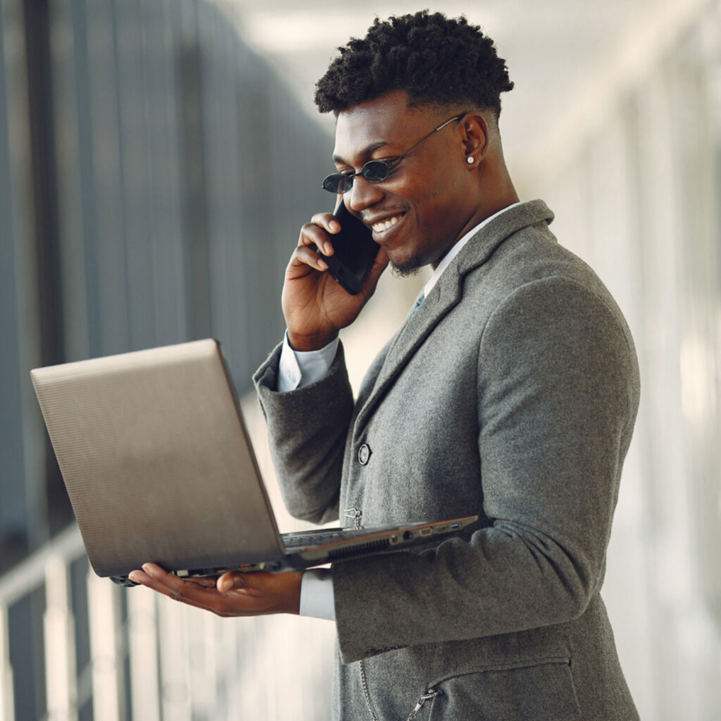 Un homme noir souriant au téléphone, en tenant son ordinateur portable dans une main